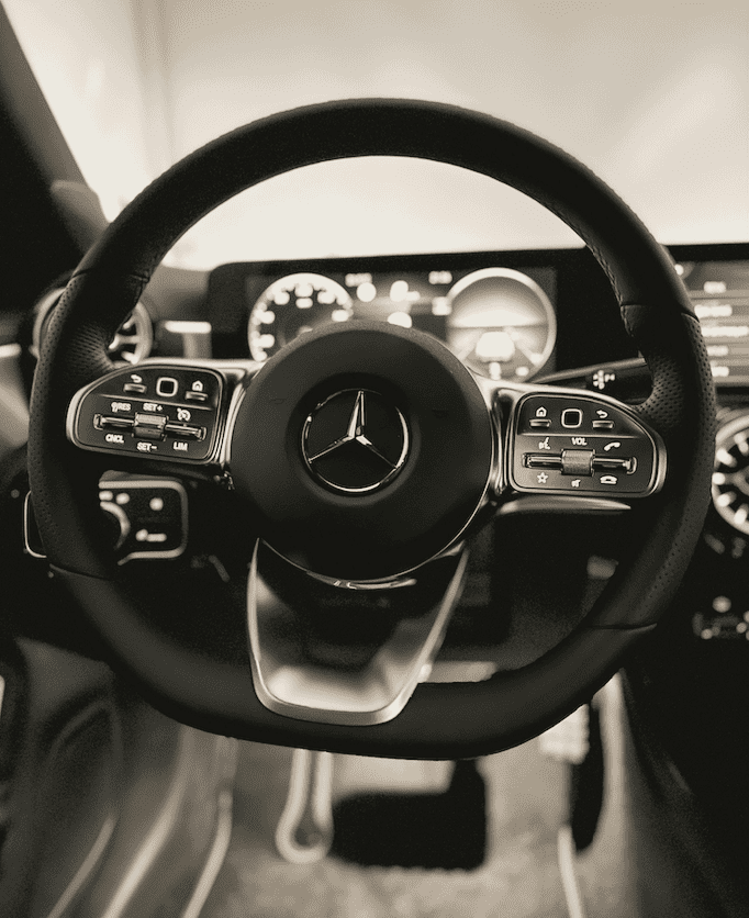High contrast black and white photo of a luxury car steering wheel and dashboard